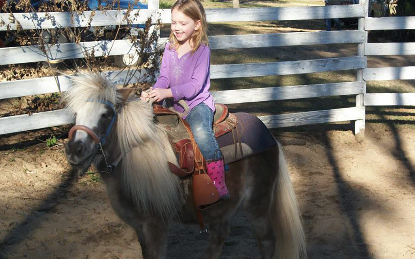 a small girl smiling while riding a pony