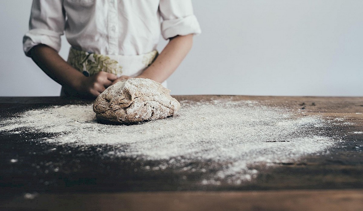 chef with bread dough on wooden table sprinkled with flour