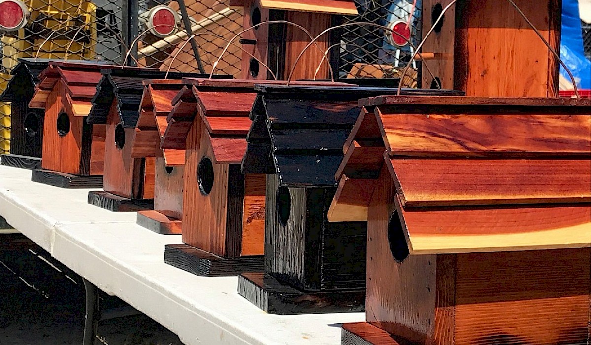 wooden birdhouses on a folding table displayed in an empty parking lot