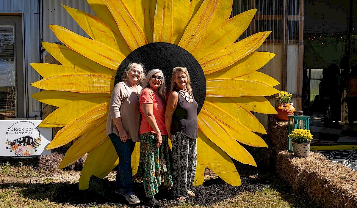 three women posing in front of a large painted sunflower photo backdrop