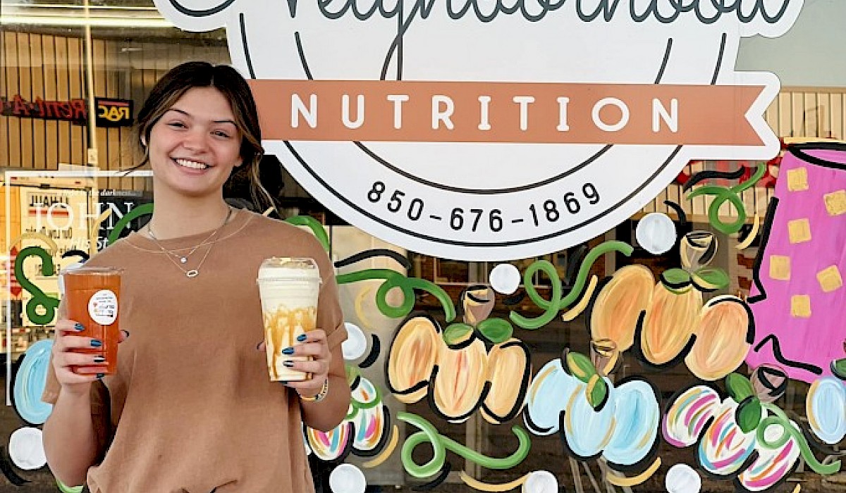 woman holding a shake and tea in front of a shake shop storefront window