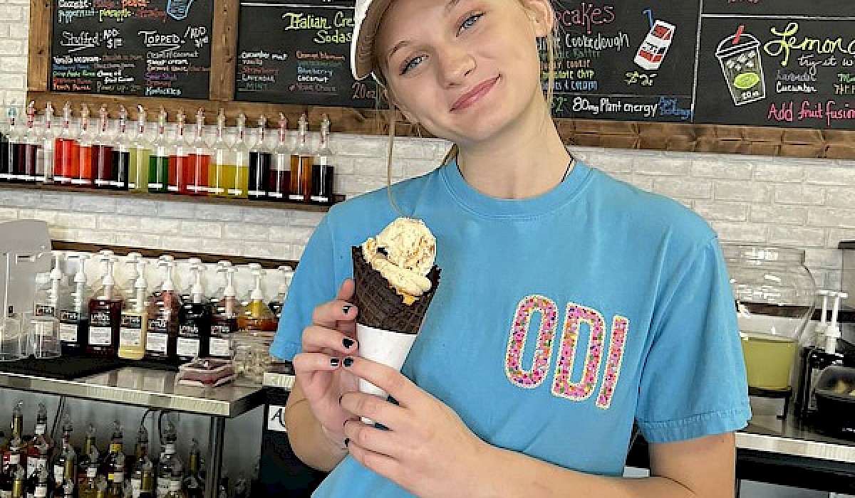 employee holding ice cream cone behind counter of dessert shop