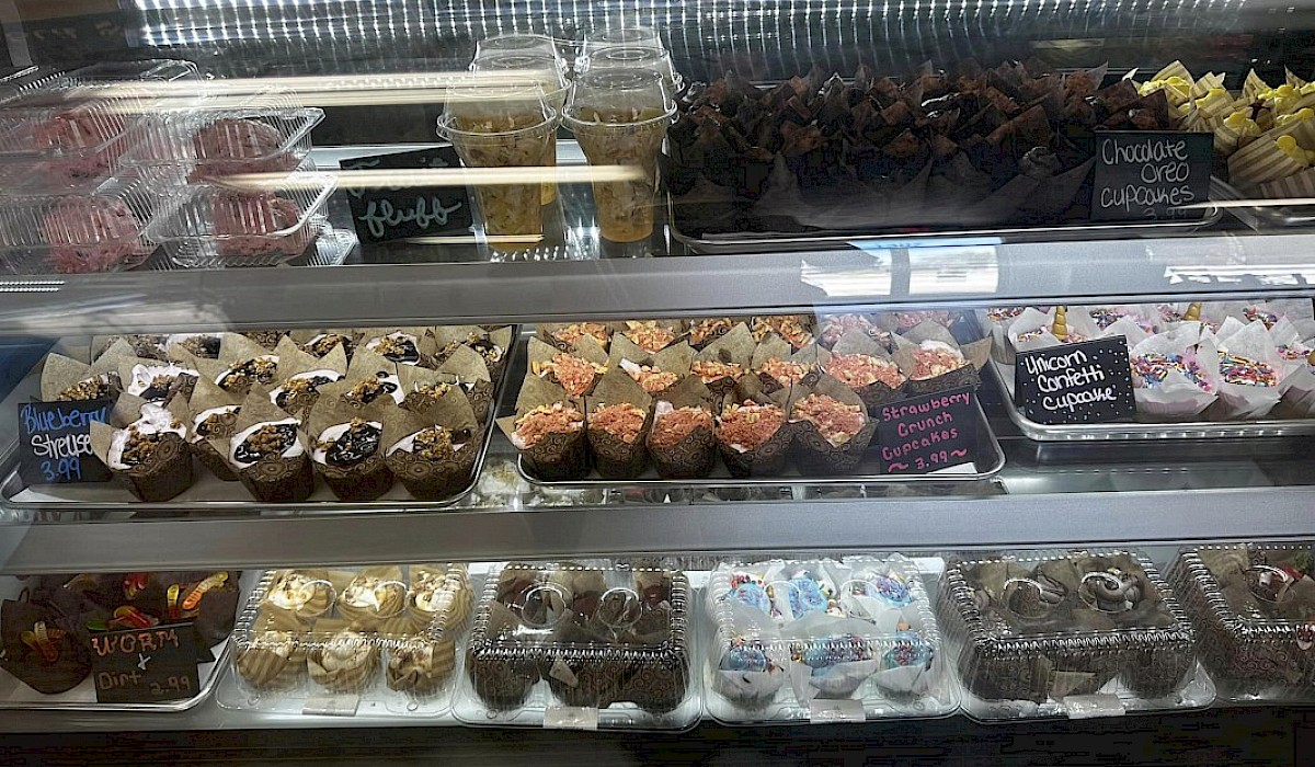 glass counter filled with custom cupcakes, brownies and cookies in dessert shop