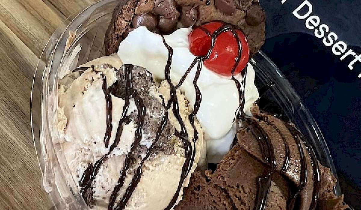 scooped ice cream in a bowl with a cookie and cherry on top on the checkout counter of a dessert shop