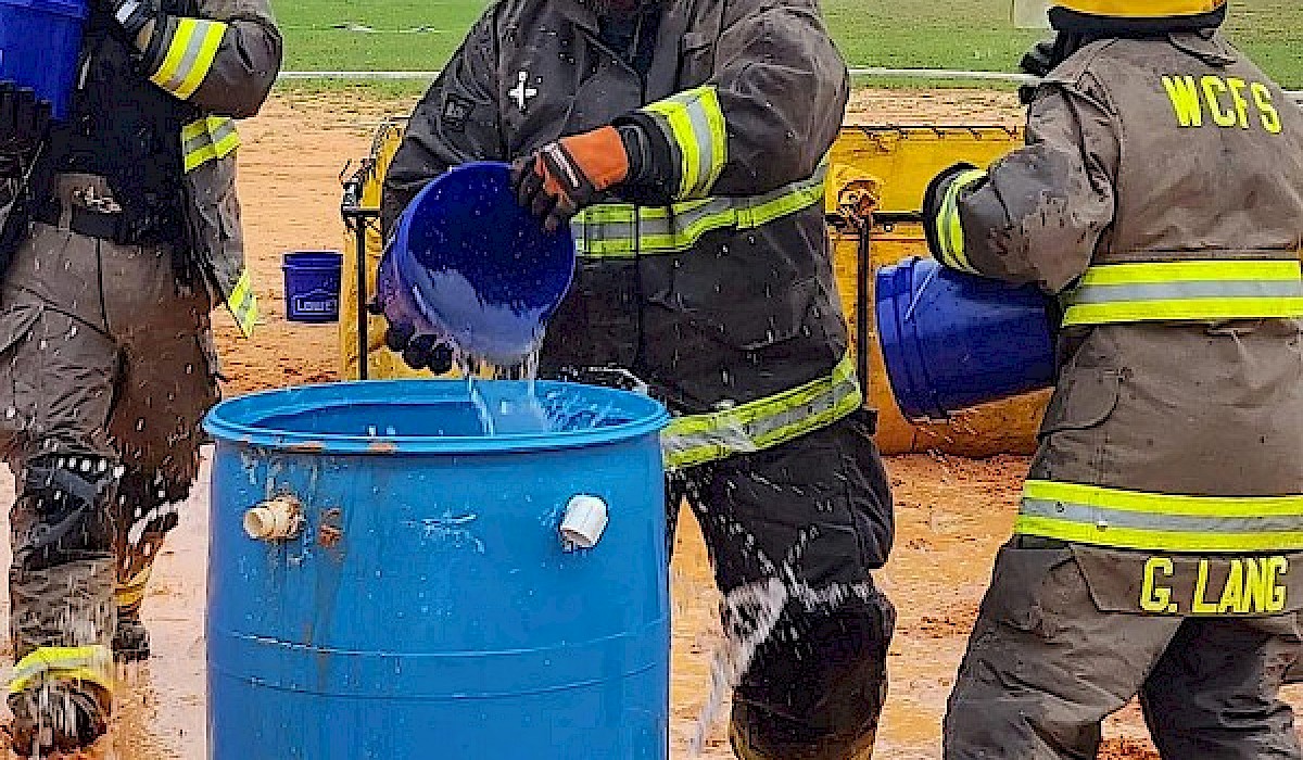 firefighters filling a water drum with water from plastic buckets during a fire game