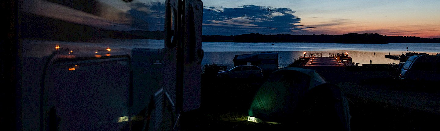an rv motorhome, and tents set up parked in front of a lake at sunset